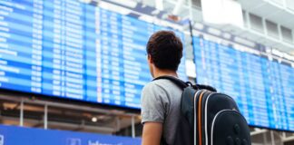 Muž na letišti s batohem, prohlíží si tabuli s informacemi