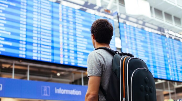 Muž na letišti s batohem, prohlíží si tabuli s informacemi
